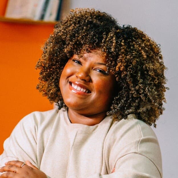 A photo of a person smiling directly at the camera with their arms crossed in front of them.